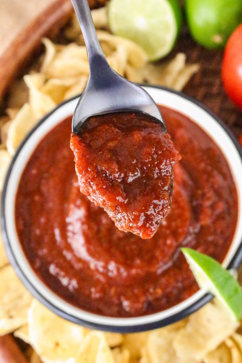 A bowl of thick blended rojo salsa on a spoon hovering over a bowl - Hostess At Heart