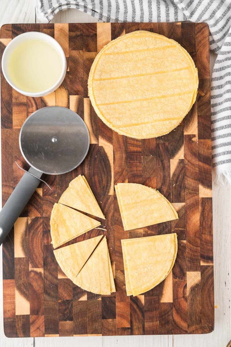 A cutting board topped with corn tortillas that are being cut into triangles - Hostess At Heart