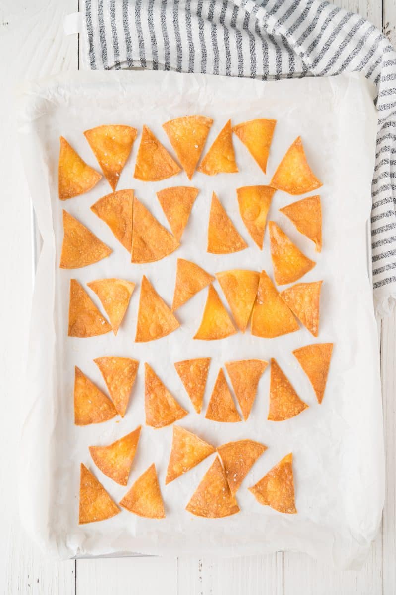 Top down view of a single layer of baked tortilla corn chips on a baking sheet - Hostess At Heart