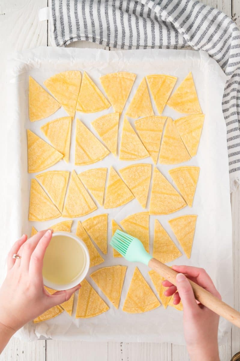 Top down view of a parchment paper-lined baking sheet filled with cut corn tortillas for making chips - Hostess At Heart
