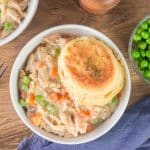 Top down view of a golden brown sourdough biscuit sitting on top of a bowl of chicken casserole made of shredded chicken and veggies - Hostess At Heart
