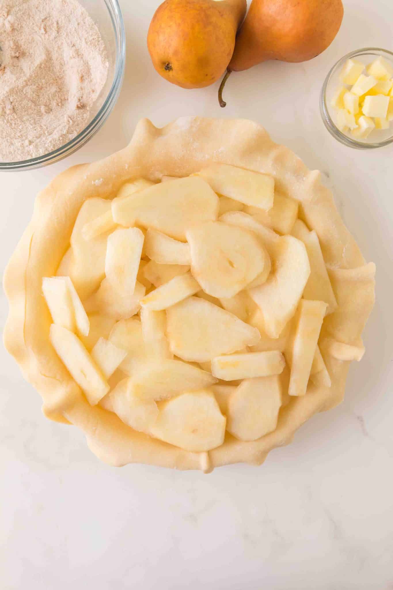 An unbaked pie shell in a pie plate topped with freshly sliced Bosc pears - Hostess At Heart