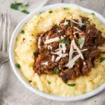 3/4 angle of a mound of rich lamb ragu sitting on a mound of cheese polenta garnished with fresh shredded parmesan - Hostess At Heart