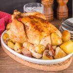 Sideview of a whole roasted chicken surrounded by potatoes - Hostess At Heart