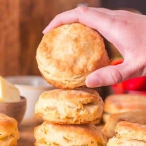 A hand holding a Sourdough Starter Biscuit that's resting on a stack of biscuits - Hostess At Heart