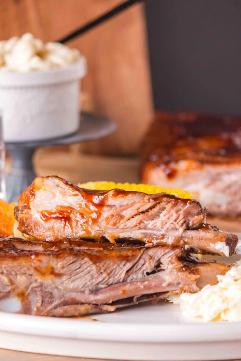 Two barbecued ribs stacked together on a dinner plate next to mashed potatoes - Hostess At Heart