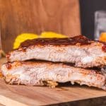 Two barbecued baby back ribs stacked together on a cutting board - Hostess At Heart