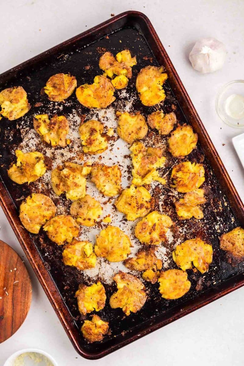 Top down view of a cookie sheet filled with crispy golden brown baked parmesan smash potatoes - Hostess At Heart