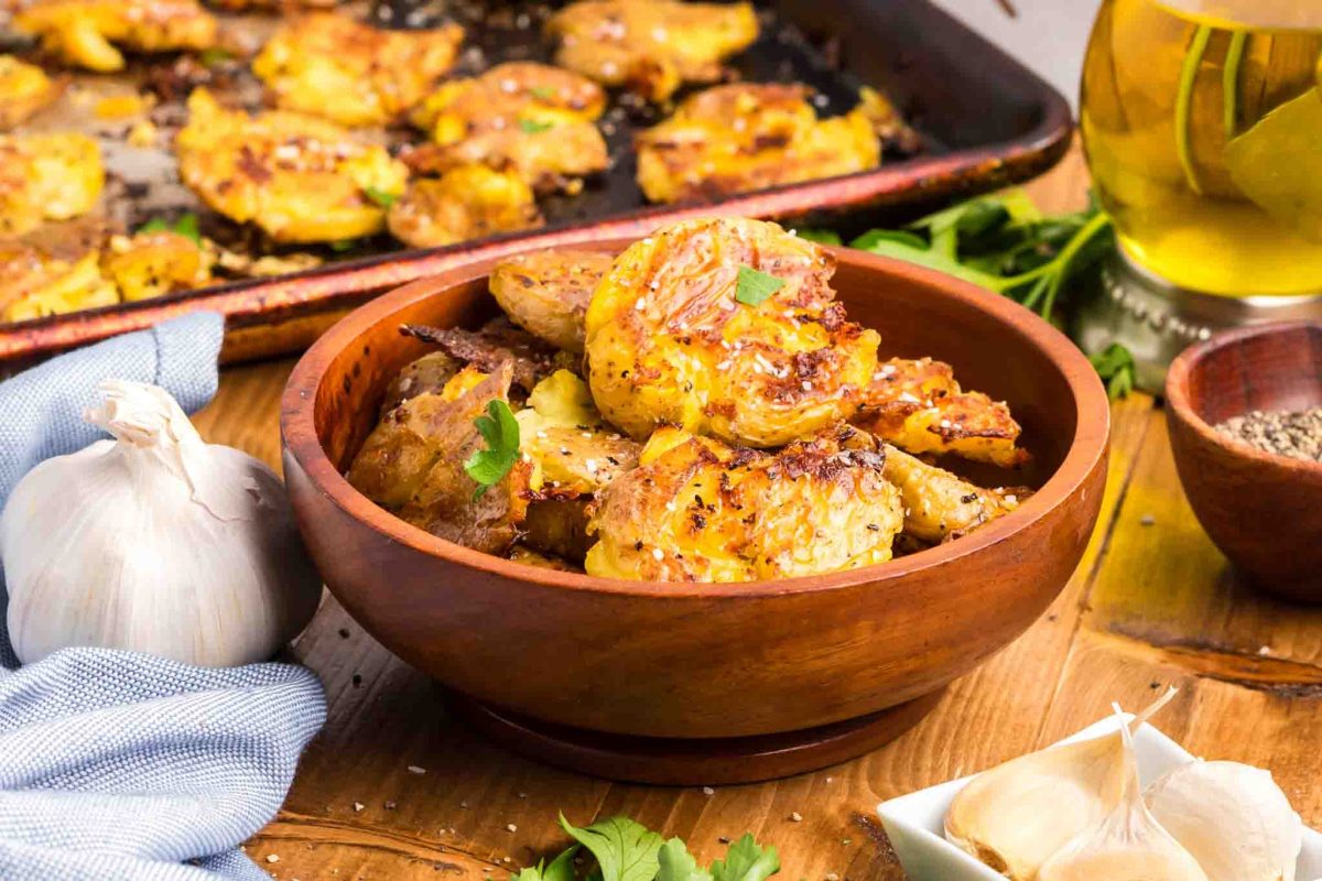 A sideview of a wooden serving bowl filled with smash potatoes with parmesan and garlic - Hostess At Heart