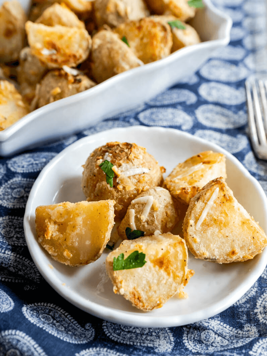Tableview of a plate filled with chunks of crispy roasted parmesan potatoes garnished with parsley - Hostess At Heart