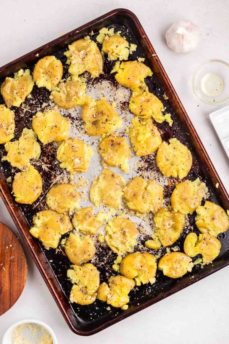 Boiled yellow yukon potatoes smashed on a baking sheet and topped with garlic, parmesan, salt, and pepper - Hostess At Heart
