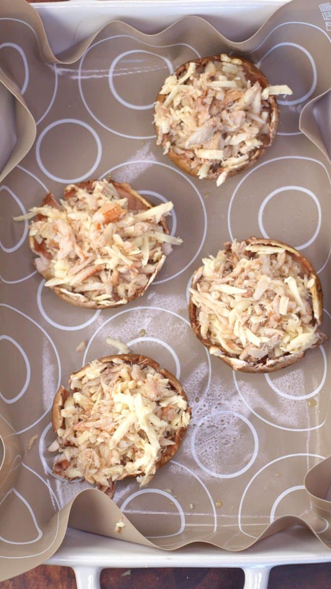 A baking dish containing 4 mushroom caps filled with crab, garlic, havarti cheese, and sun dried tomatoes - Hostess At Heart