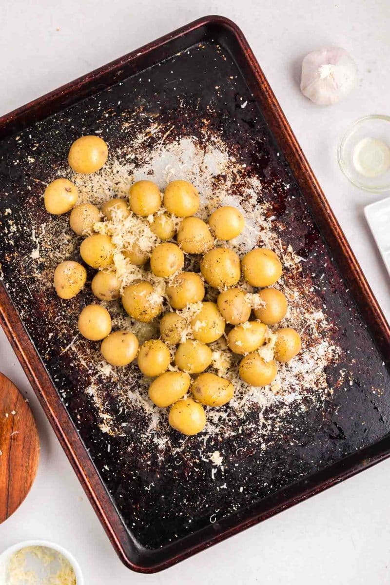 A sheet pan topped with small yellow potatoes that have been topped with minced garlic and fresh parmesan. Hostess At Heart