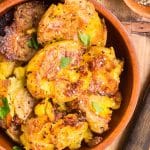A closeup angled view of baked potatoes smashed with parmesan in a bowl - Hostess At Heart
