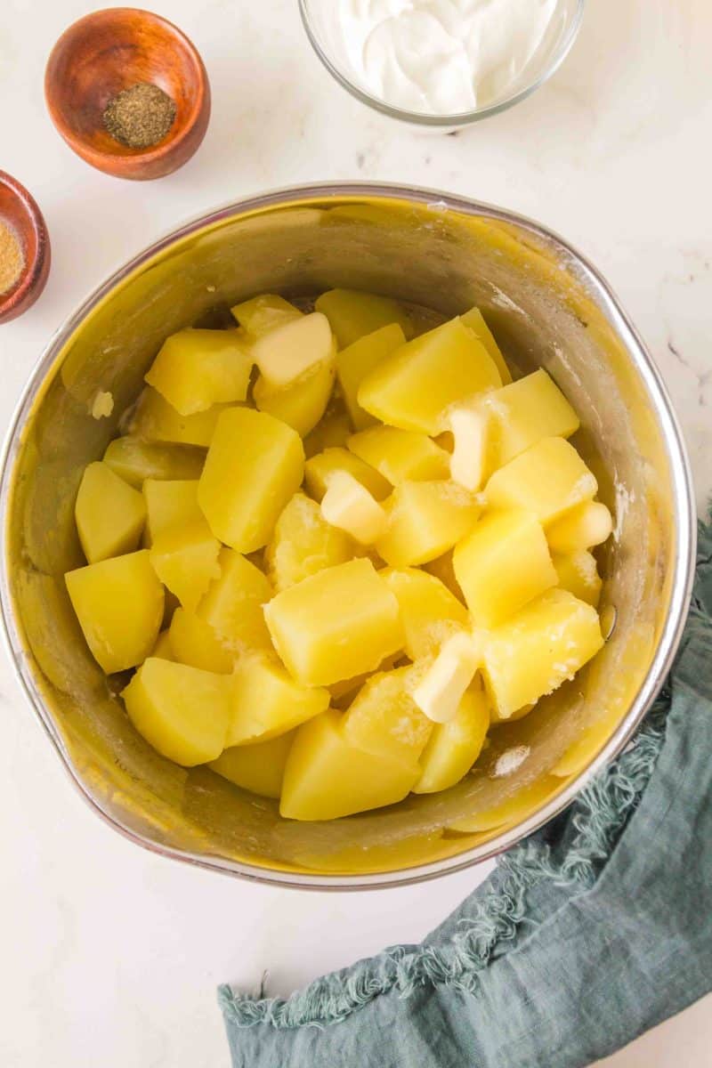 Top down view of the bowl of an electric mixer filled with cooked yukon potatoes and butter before mashing - Hostess at Heart
