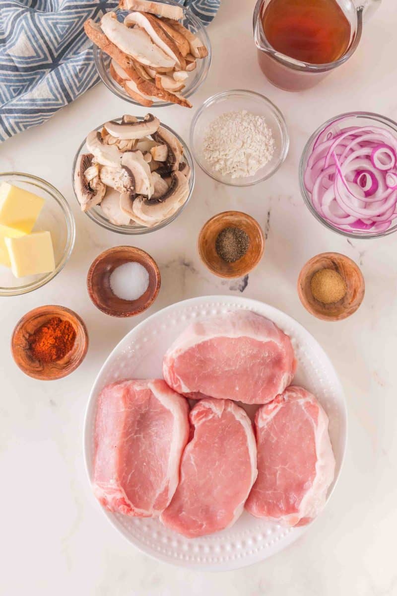 Ingredients to make cast iron pork chops: 4 pork loin chops, mushrooms, onions, flour, butter, paprika, salt, pepper, and garlic powder - Hostess At Heart
