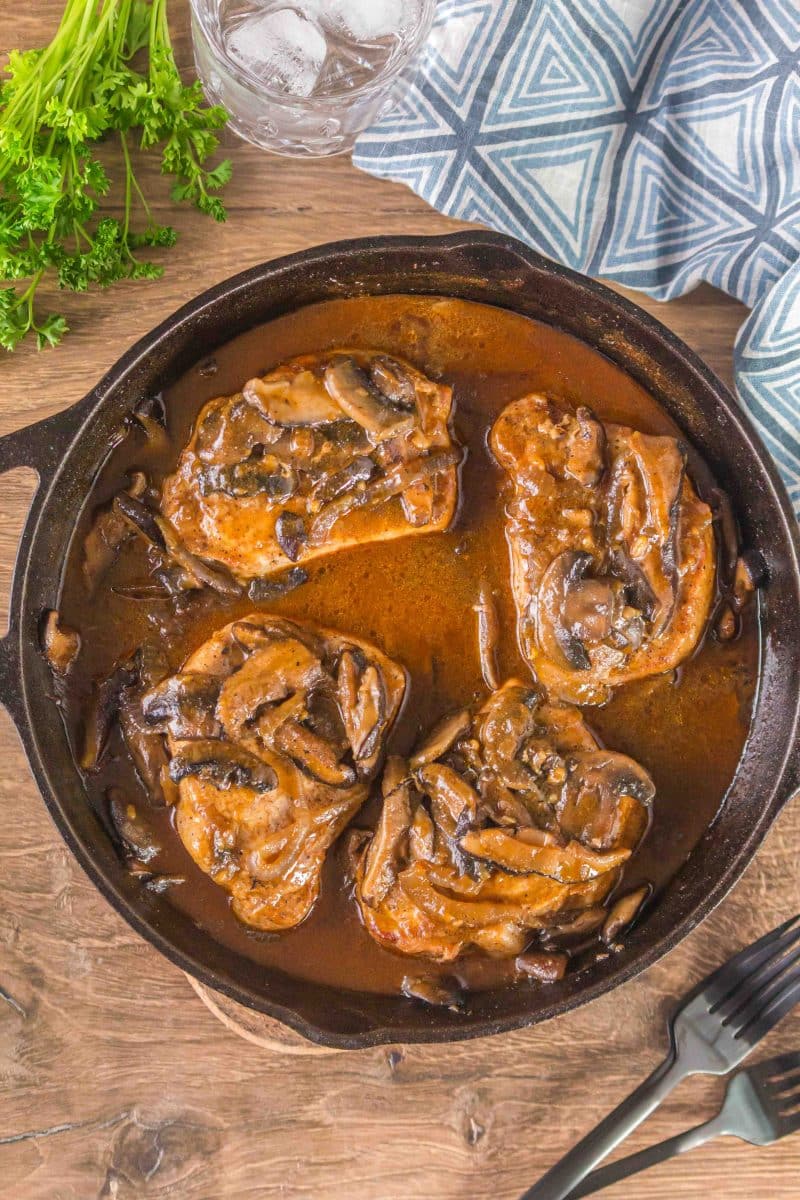 Top down view of a cast iron skillet filled with four pork loin chops covered with mushroom gravy - Hostess At Heart