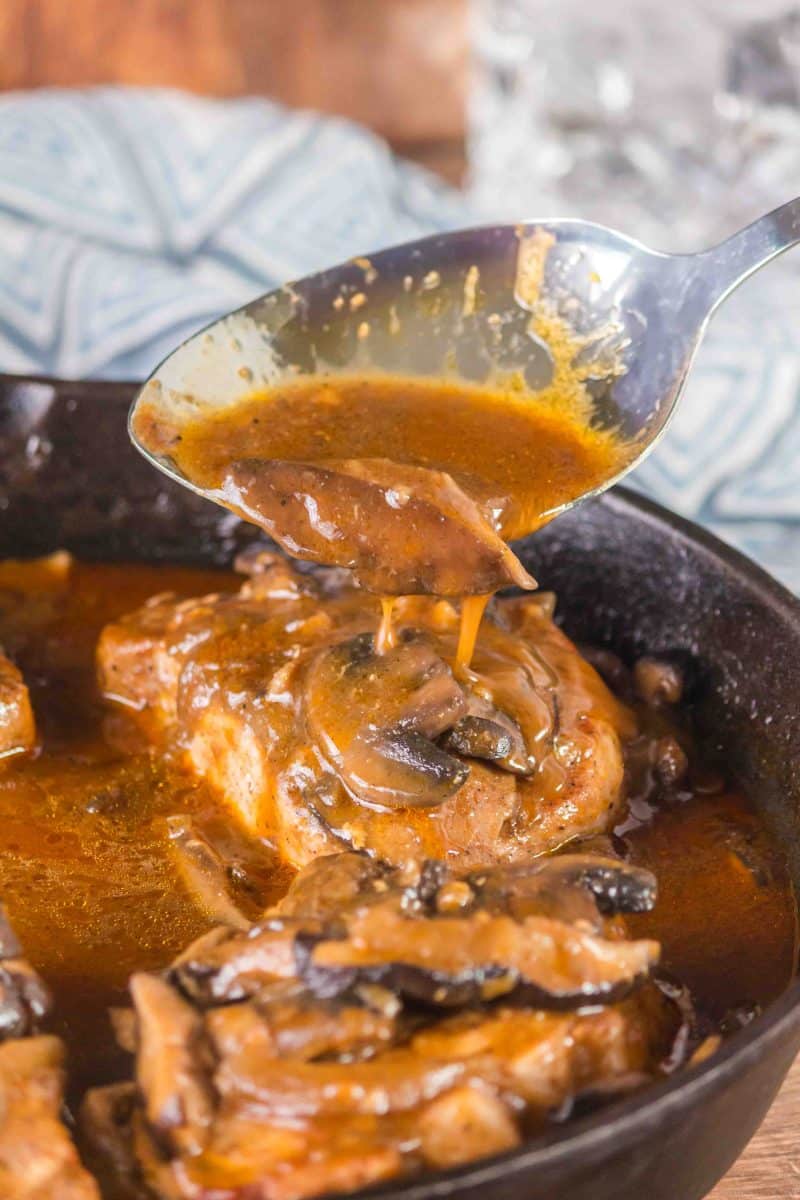 A spoon drizzling gravy over a cooked mushroom onion pork chop - Hostess At Heart