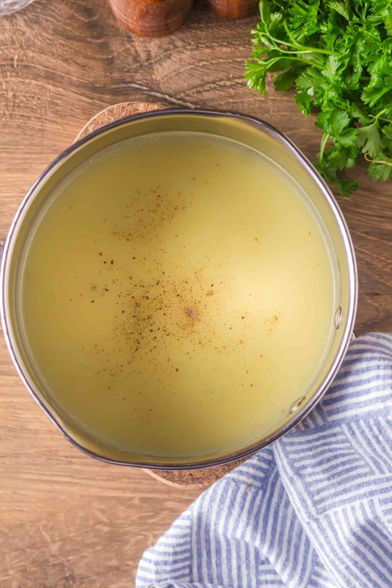 Salt and pepper added to a pot of smooth and creamy chicken gravy in a pot - Hostess At Heart