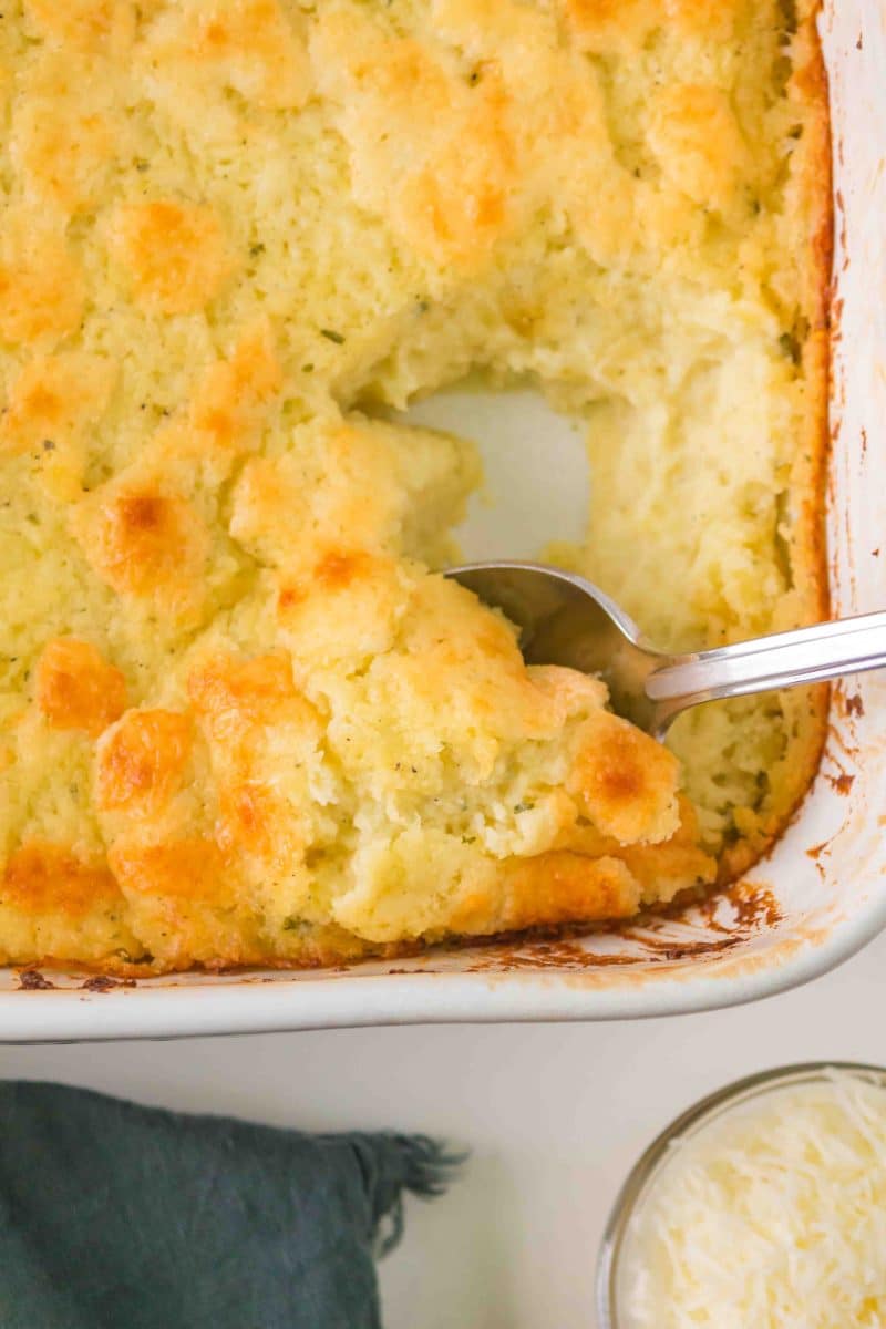 A spoon lifting out a serving of creamy mashed potatoes from the casserole dish - Hostess At Heart