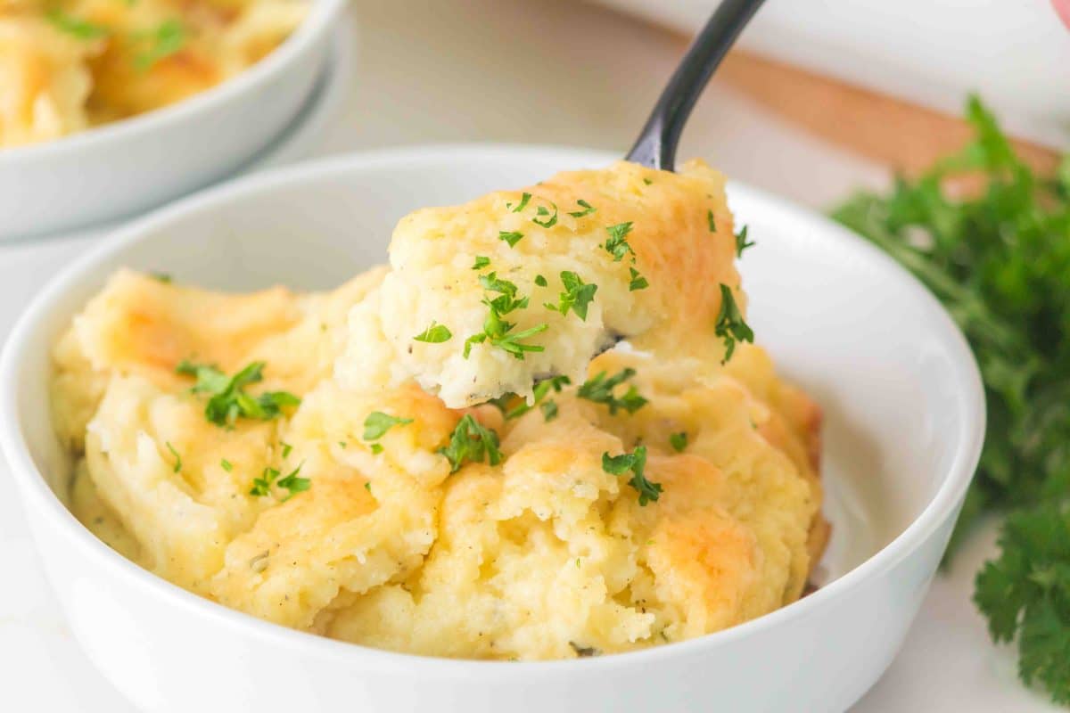 Side view of a spoon lifting a serving of Boursin Mashed Potatoes from the bowl - Hostess At Heart