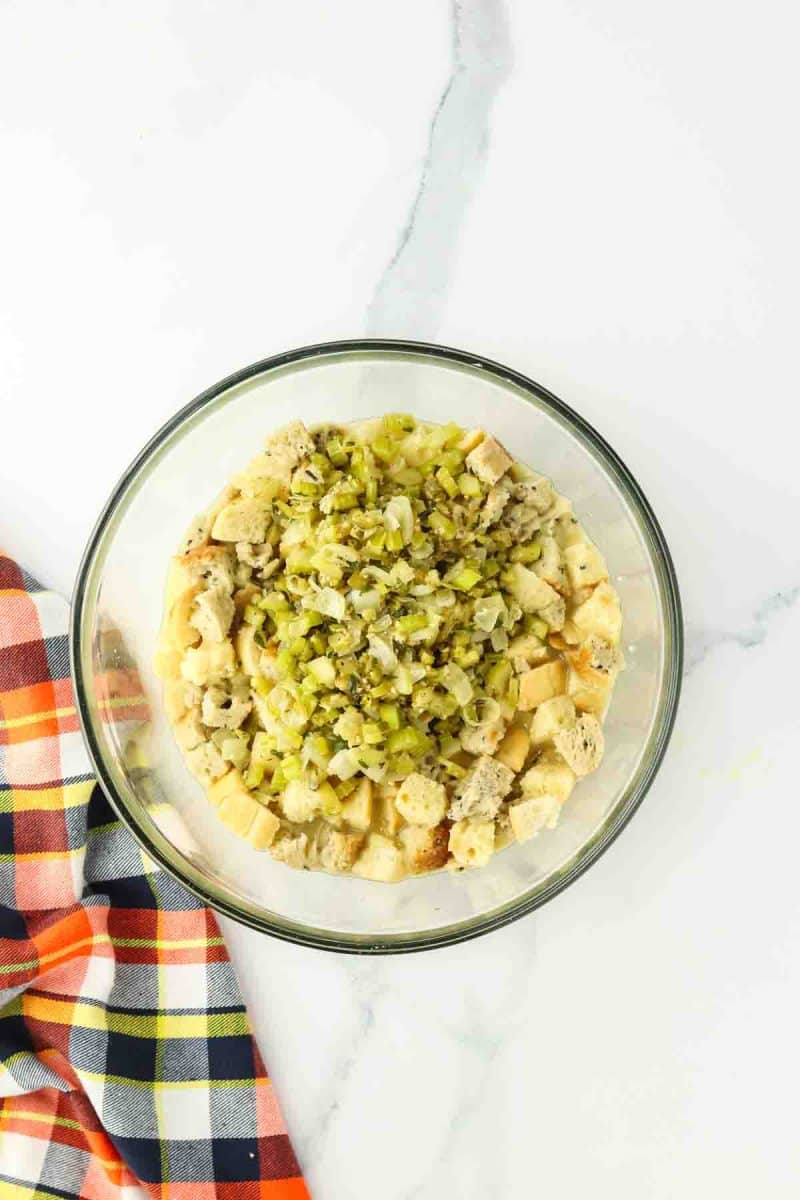 Toasted bread cubes mixed with sauteed veggies in a mixing bowl - Hostess At Heart