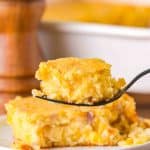 Table view of a serving of corn scallop casserole with a fork hovering over the dish filled with a bite of the corn casserole - Hostess At Heart