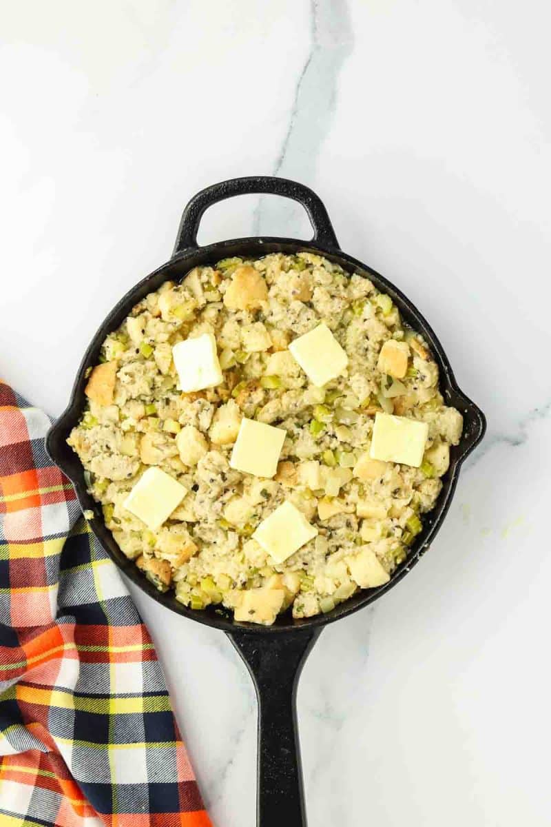 An unbaked Thanksgiving skillet stuffing topped with pads of butter - Hostess At Heart