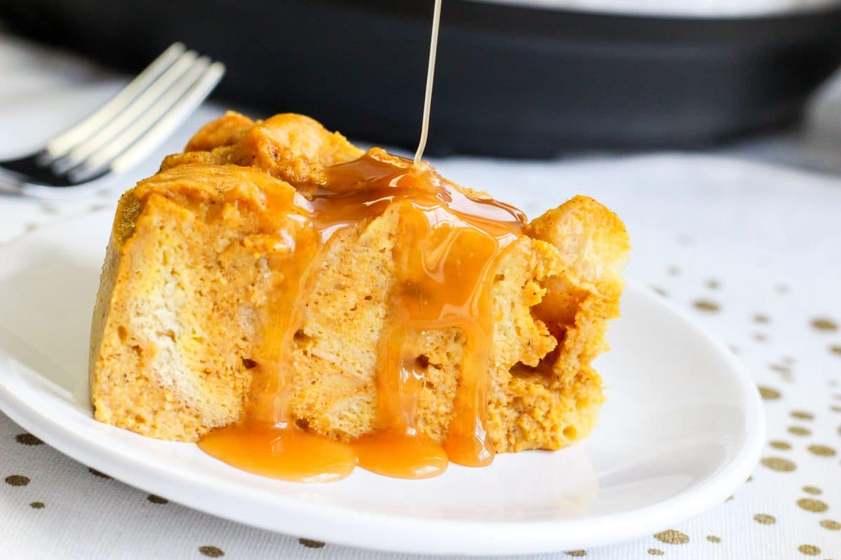 A plate holding a slice of bread pudding that's being drizzled with caramel sauce - Hostess At Heart