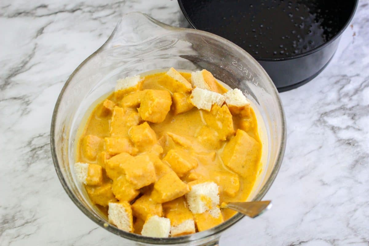 A bowl filled with cubes of bread that are covered in a pumpkin bread pudding batter.