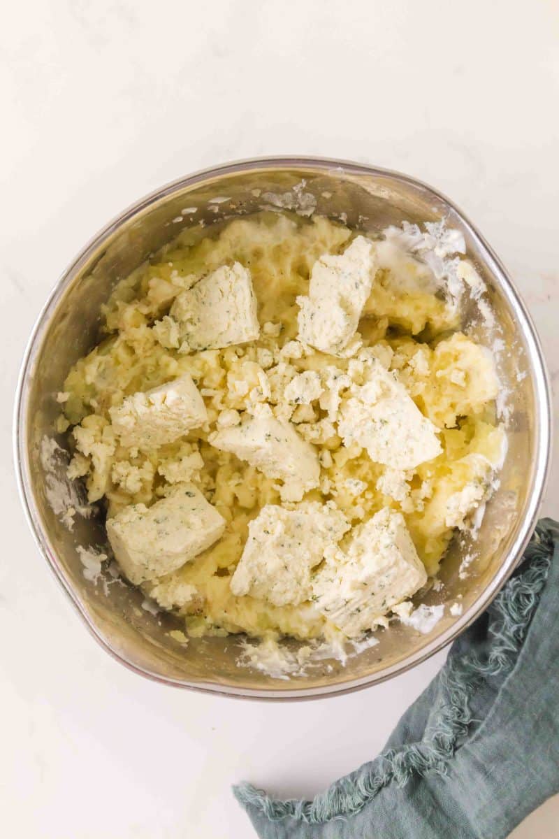 The bowl of an electric mixer filled with mashed potatoes, butter, sour cream, and boursin cheese - Hostess At Heart