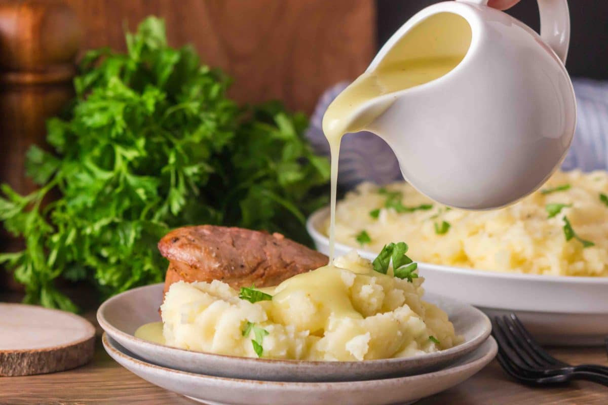A sideview showing a gravy boat pouring thick and creamy chicken gravy over mashed potatoes - Hostess At Heart