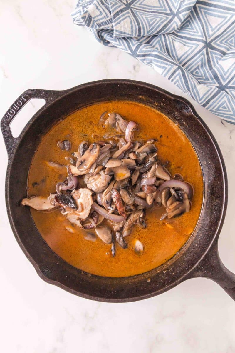 Cooked mushrooms added to gravy in a cast iron skillet - Hostess At Heart