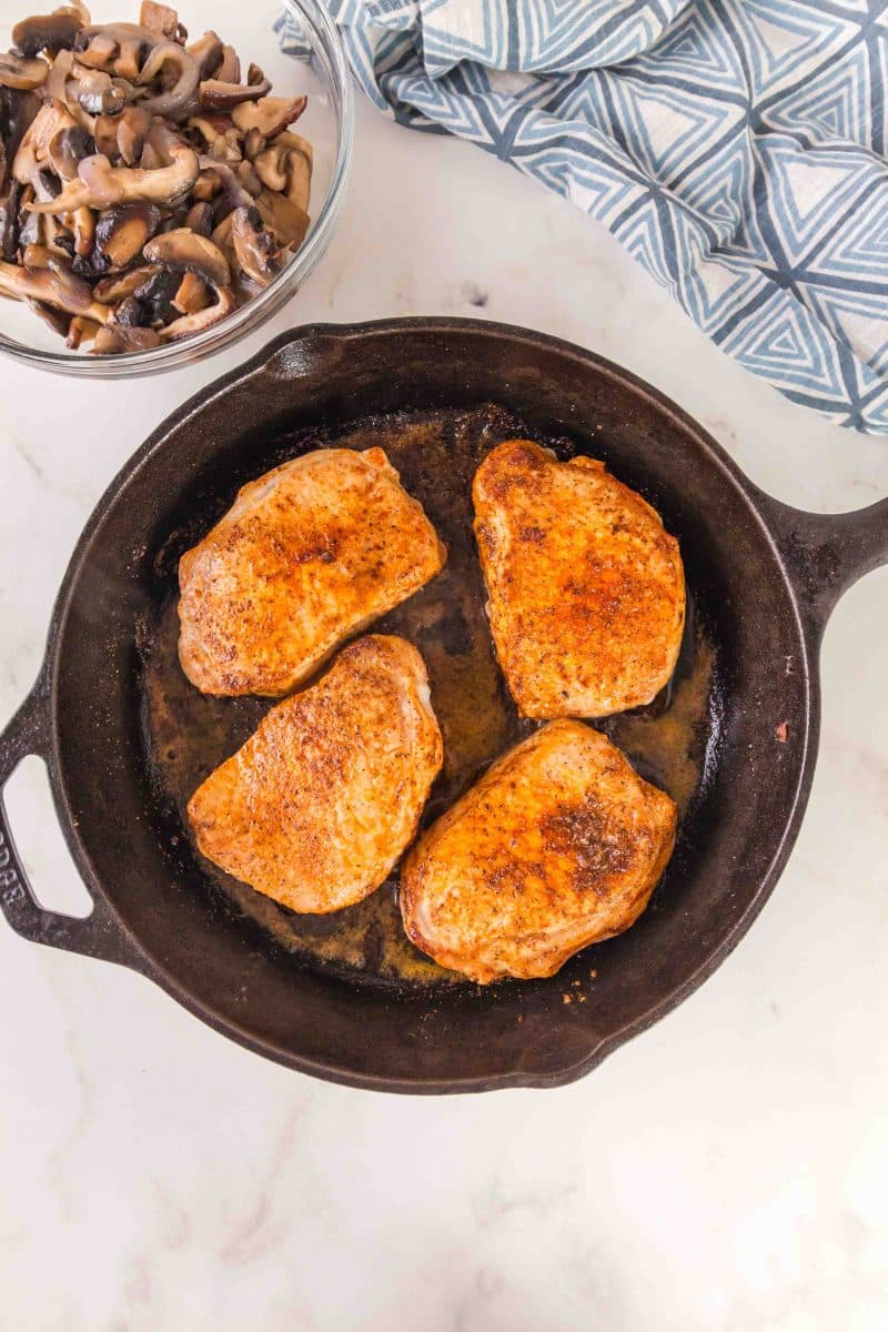 A cast iron skillet containing 4 seared boneless pork chops - Hostess At Heart