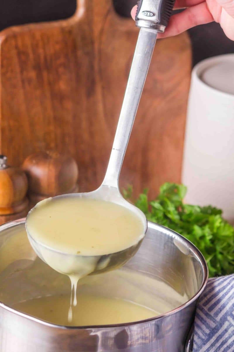 Sideview of a ladle lifting creamy chicken gravy without drippings from a pot. Hostess At Heart