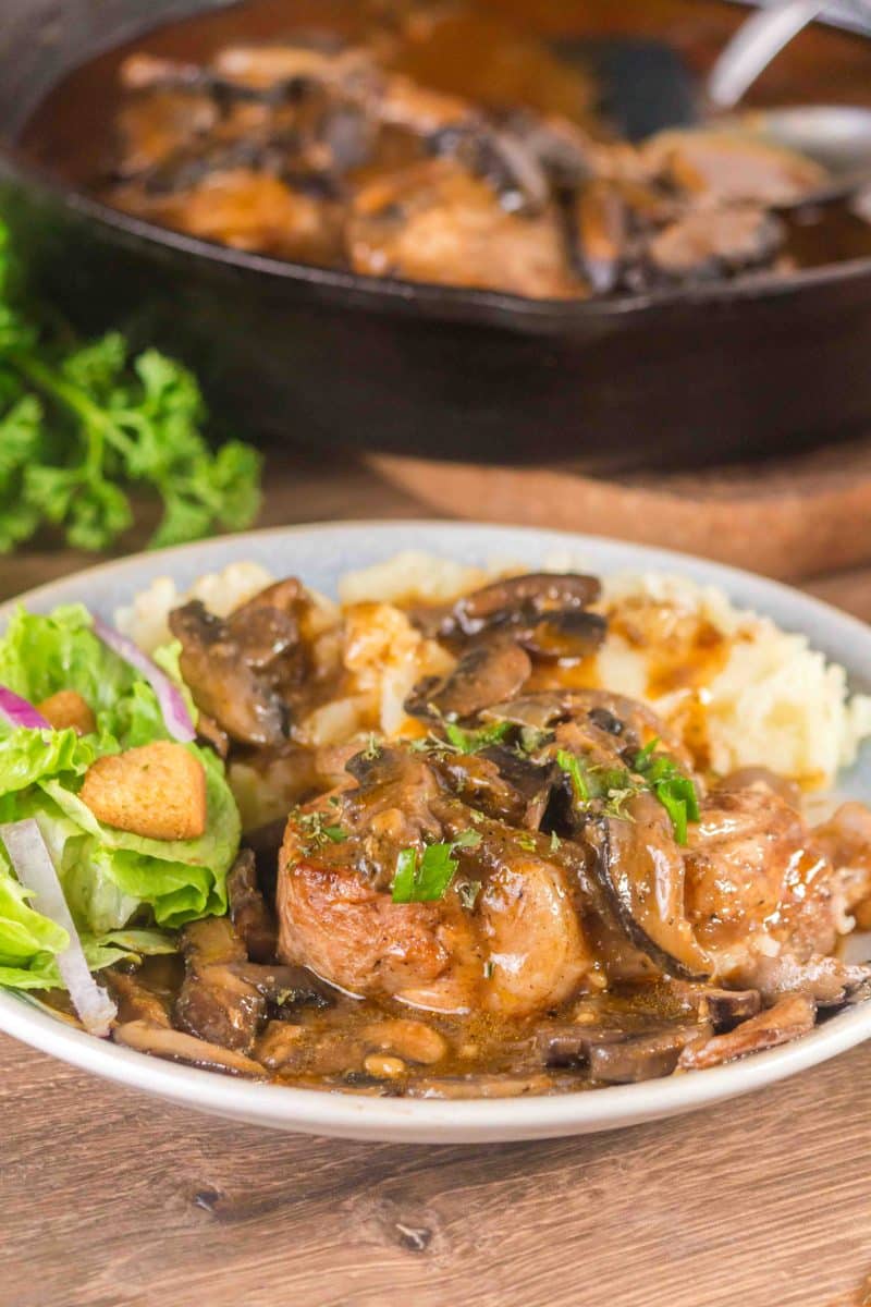 Angled view of a cast iron cooked pork chop topped with mushroom onion gravy - Hostess At Heart