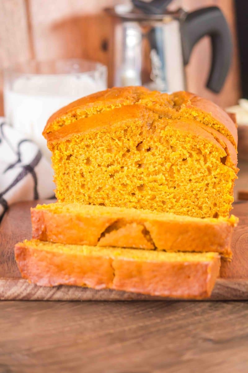 Front view of a partially sliced loaf of sourdough discard pumpkin bread. The slices are fanned in front of the sliced loaf - Hostess At Heart