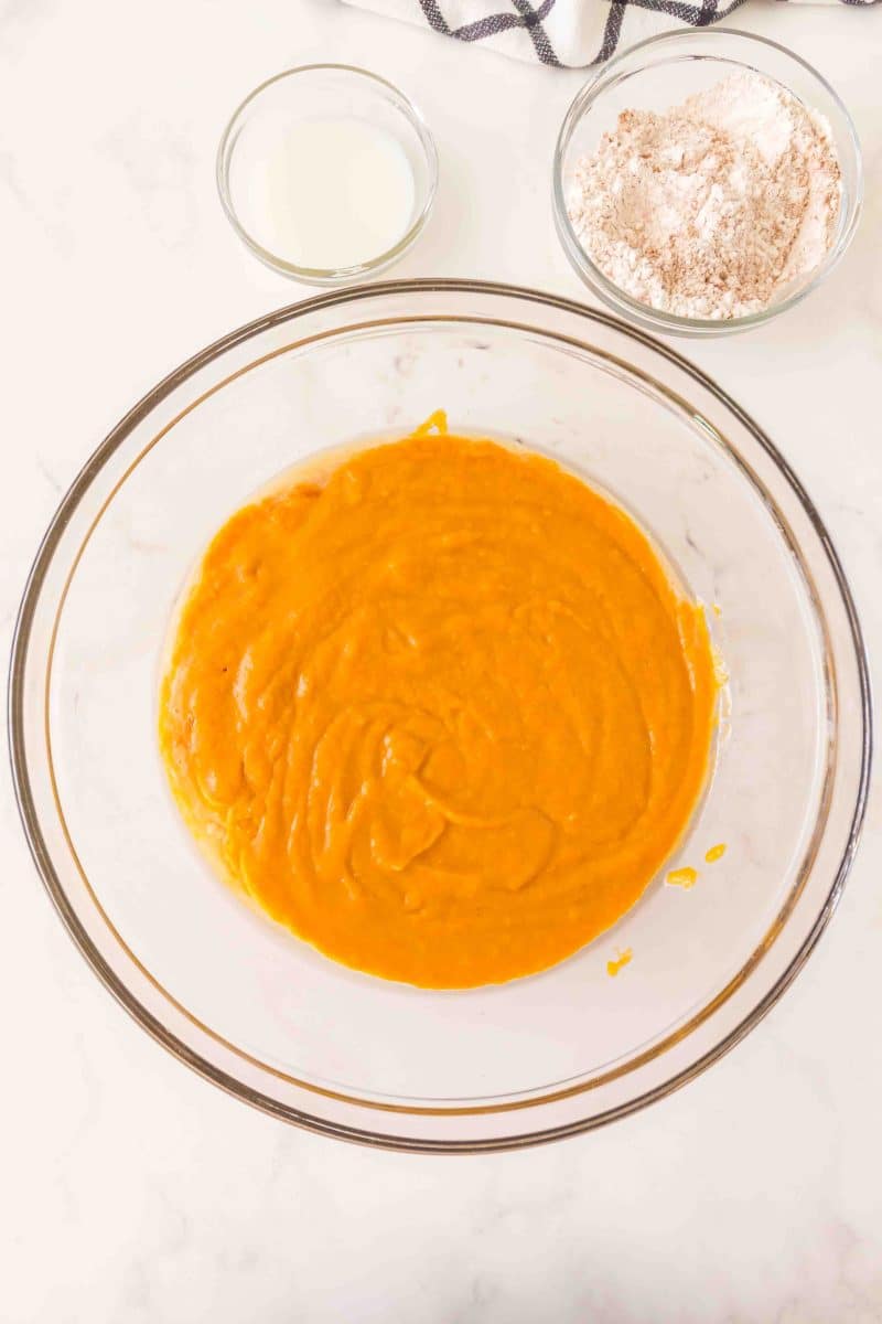 Top down view of pumpkin puree added to a bowl containing a mixture of egg, sourdough discard, brown sugar, white sugar, vanilla, and oil. Hostess At Heart