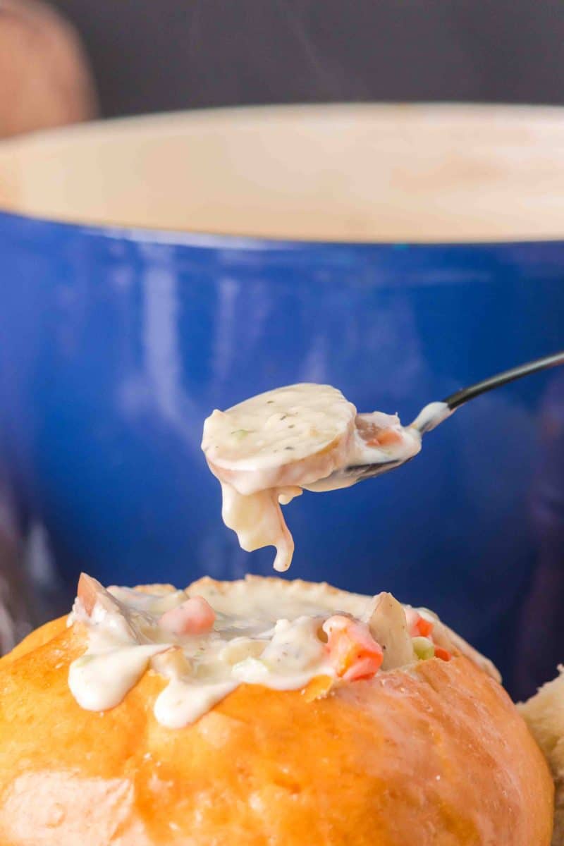 A spoon lifting a large bite of clam chowder with potatoes from a bread bowl filled with the soup. Hostess At Heart
