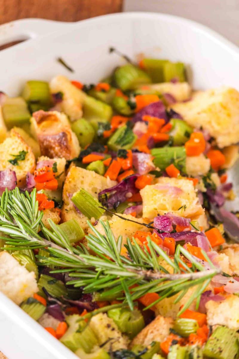 Close up of homemade sourdough stuffing with crispy golden top and tender herb-filled interior. A sprig of fresh rosemary garnishes the top - Hostess At Heart