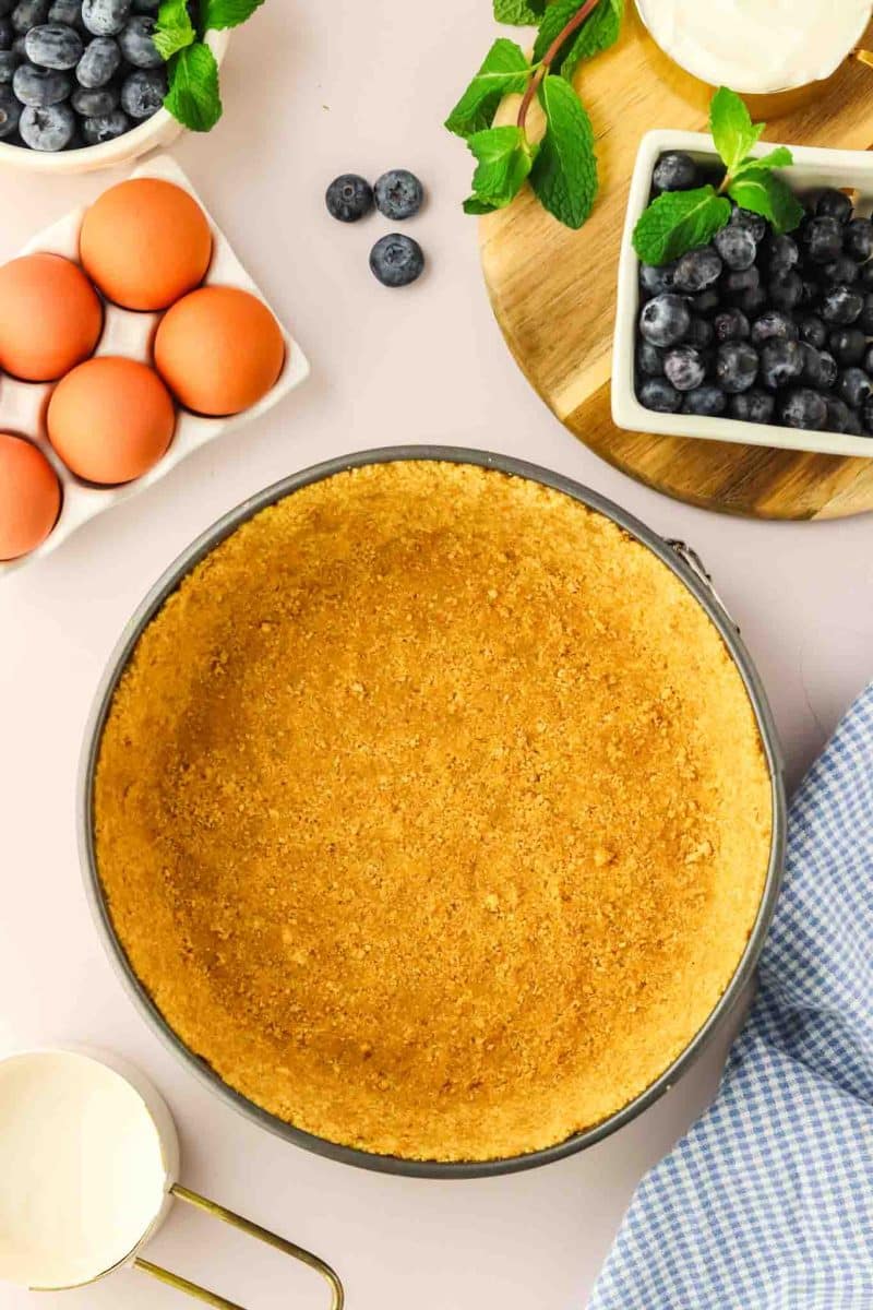 Golden brown baked graham cracker crust in springform pan ready for blueberry cheesecake filling - Hostess At Heart