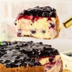Creamy slice of blueberry cheesecake on spatula showing graham cracker crust and blueberry-studded filling - Hostess At Heart