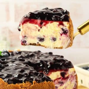 Creamy slice of blueberry cheesecake on spatula showing graham cracker crust and blueberry-studded filling - Hostess At Heart