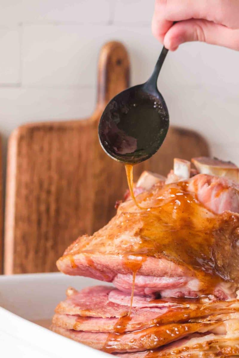 Spooning brown sugar glaze onto spiral ham with for caramelizing - Hostess At Heart