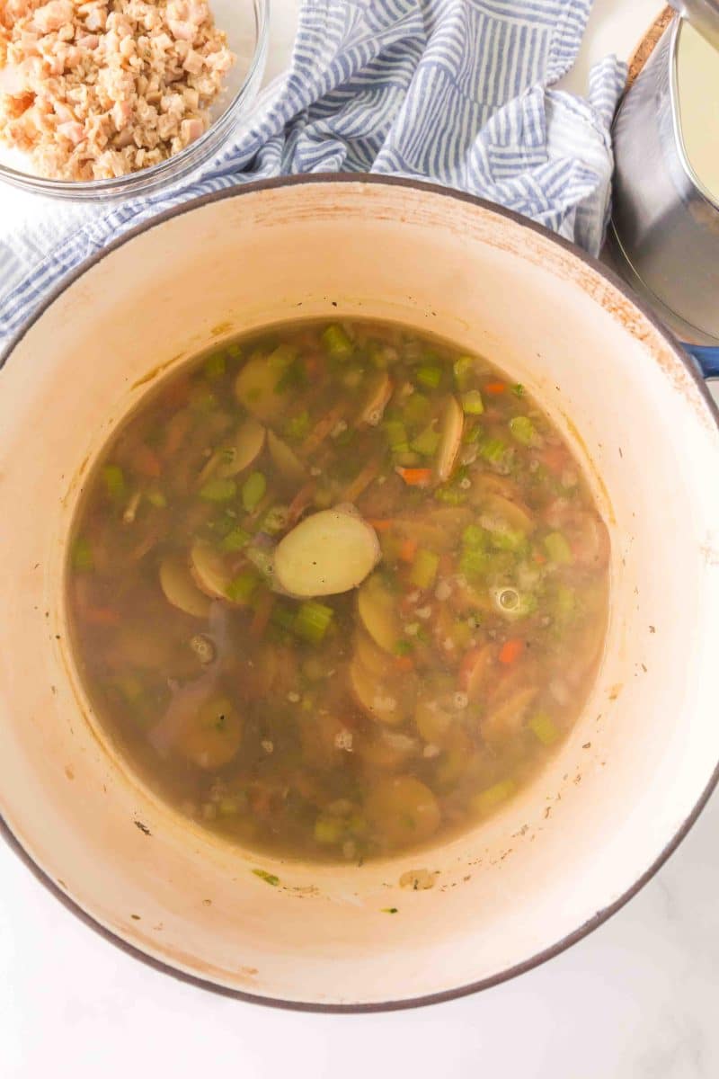 A soup pot filled with carrots, celery, onions, spices, potatoes, chicken broth and claim juice. Hostess At Heart