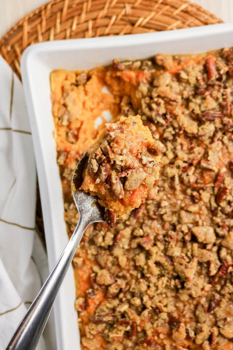 Close-up of a spoon with a serving of sweet potato casserole made from canned yams and topped with a crusty pecan layer - Hostess At Heart