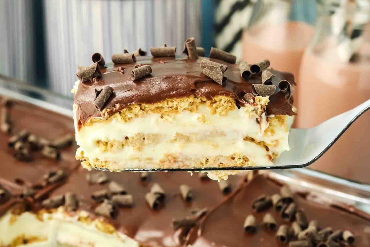 Slice of chocolate eclair cake on a spatula showing layers of graham crackers, vanilla pudding, and chocolate frosting - Hostess At Heart