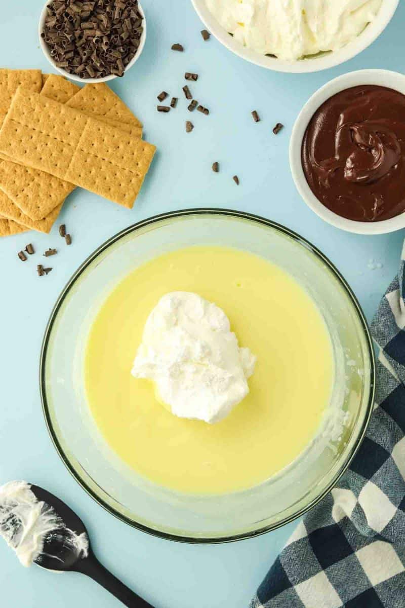 Folding whipped topping into vanilla pudding mixture for chocolate eclair cake - Hostess At Heart