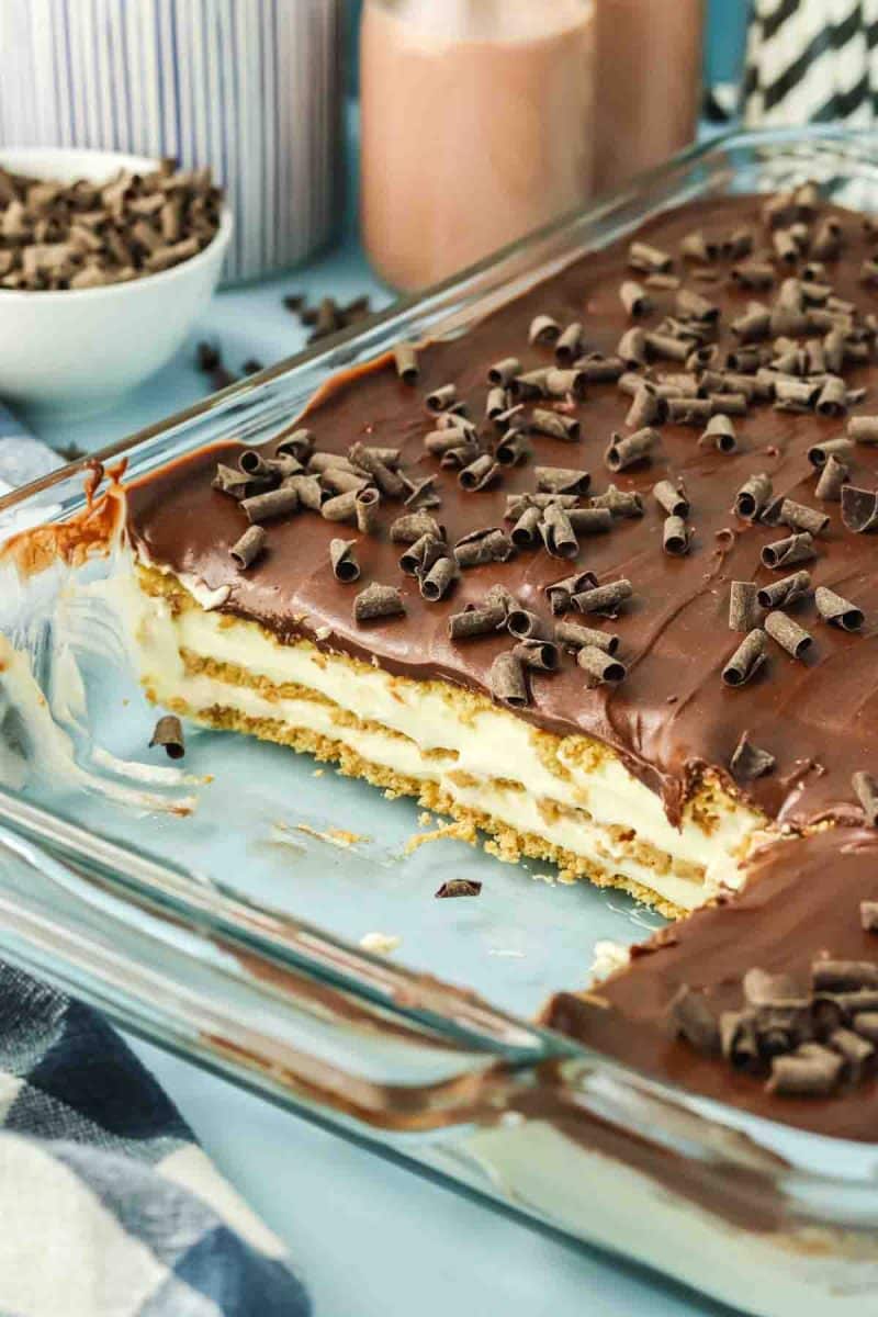 Close-up of a pan of no-bake eclair cake sliced and showing creamy pudding layers between softened graham crackers. Hostess At Heart