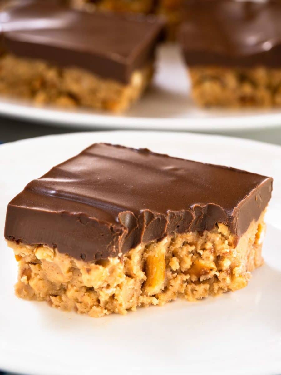 Table view image of a single peanut butter pretzel bar on white plate with chocolate topping and a bite taken out of it - Hostess At Heart